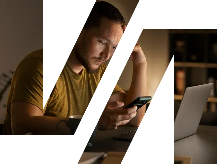 Homem preocupado olha o celular à noite, sentado diante do notebook