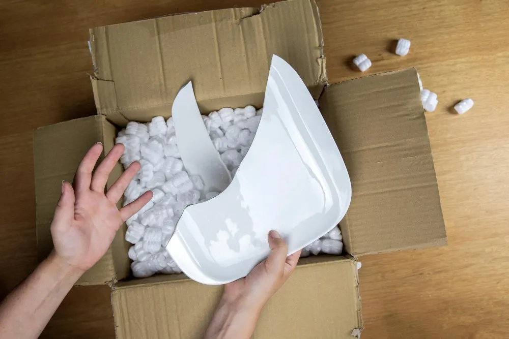 Pessoa abre uma caixa de papelão e encontra um prato quebrado