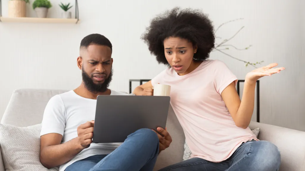 Casal no sofá olha o notebook com expressão de indignação