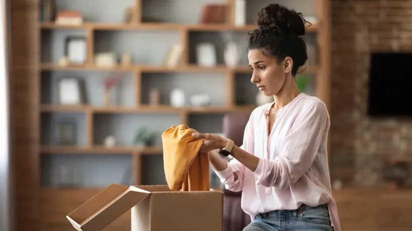 Mulher tira uma peça de roupa de uma caixa de encomenda e a examina
